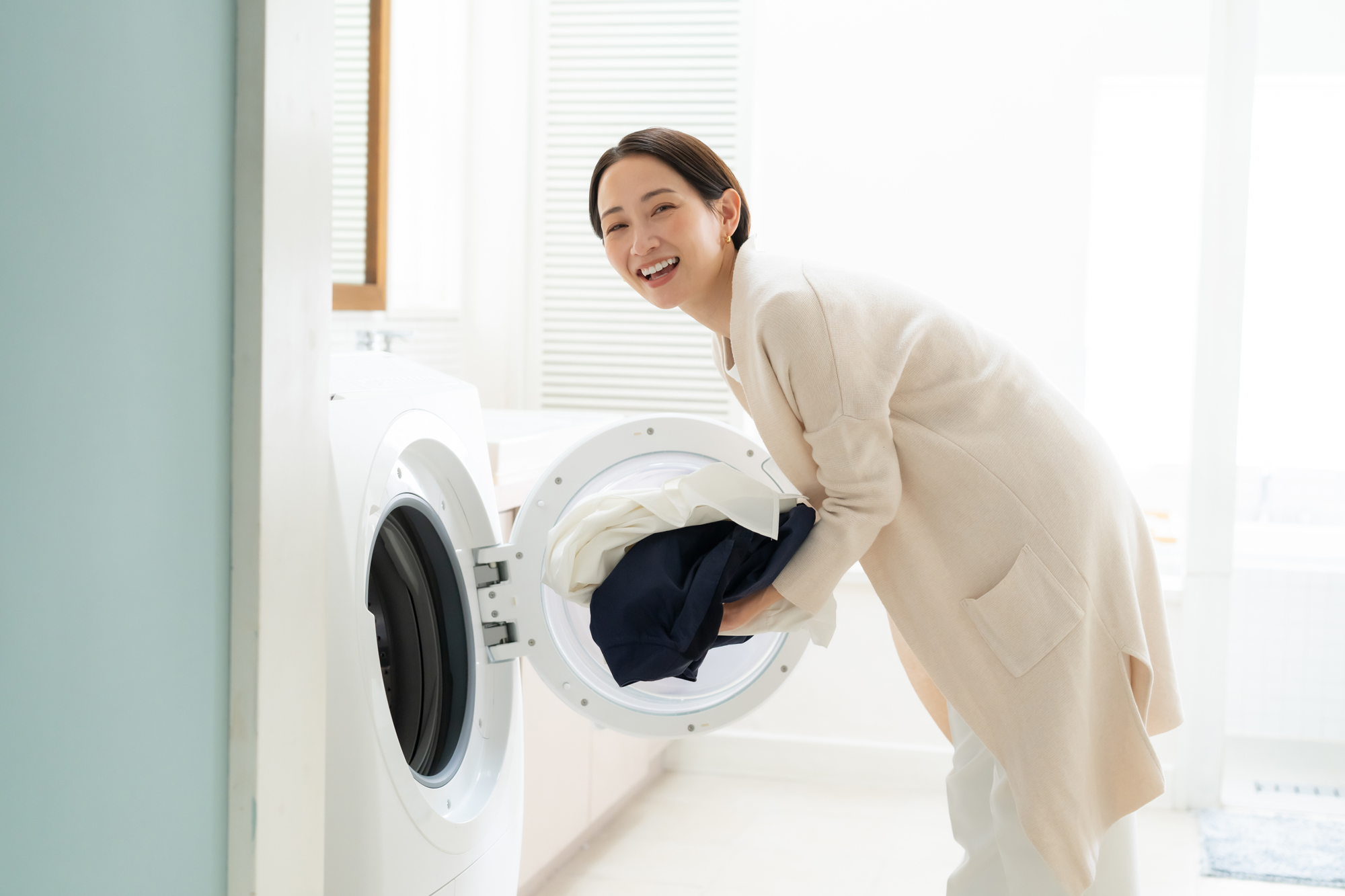 笑顔で洗濯物を洗濯機に入れる女性