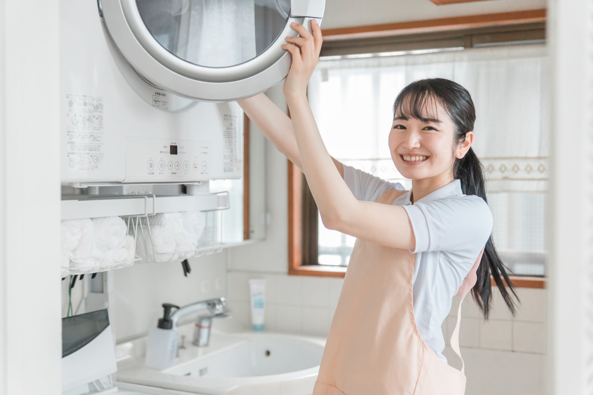 洗濯機の上に設置された衣類乾燥機を開ける女性